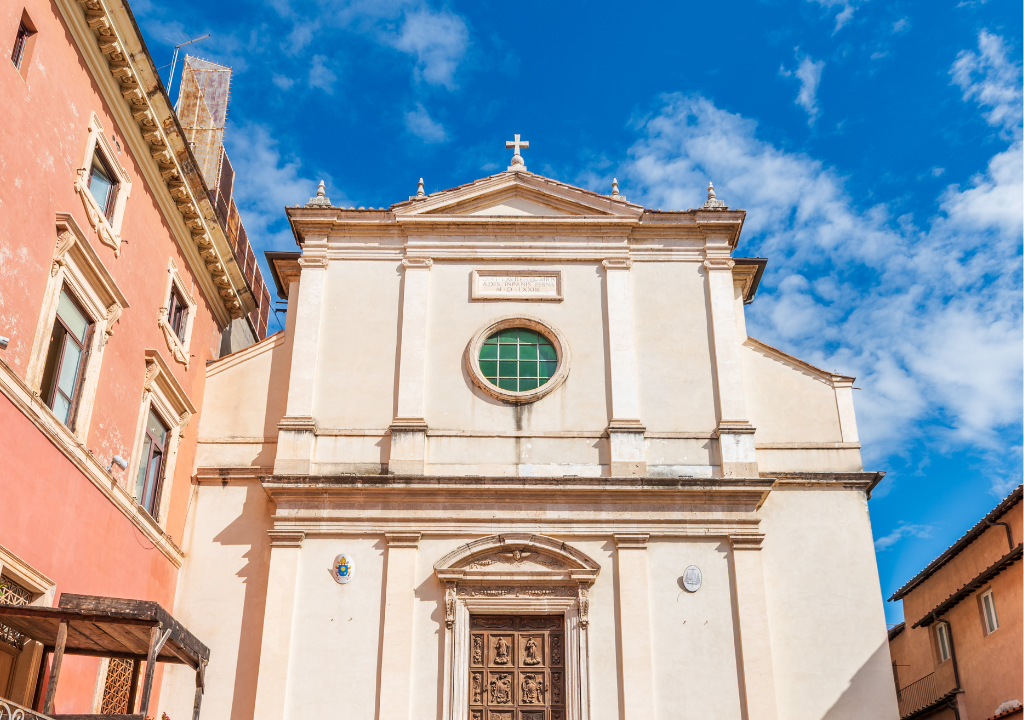 l'immagine rappresenta la chiesa di San Lorenzo in Panisperna, una chiesa dalla facciata molto semplice color panna on un rosone verde e una porta in legno.