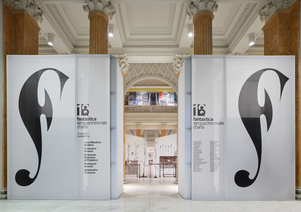 l'immagine rappresenta lo spazio espositivo con 2 pannelli laterali con il logo dell'evento e i nomi degli artisti, infondo si intravedono le opere.