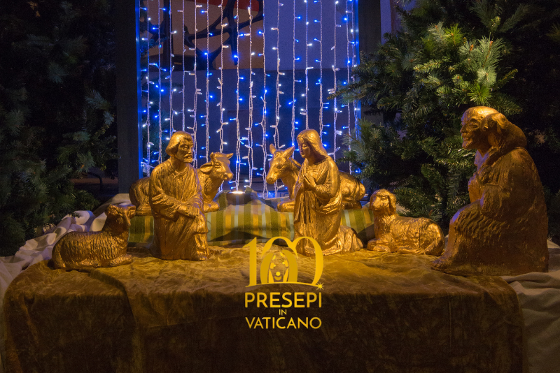 l'immagine rappresenta un presepe handmade con le sagome oro, dietro una tenda di luci di natale e sfondo blu