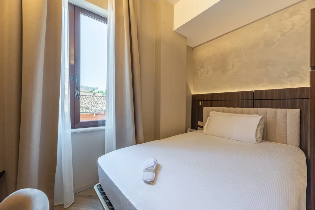 Camera matrimoniale dell’Hotel Raffaello con letto, finestra e vista sui tetti della città